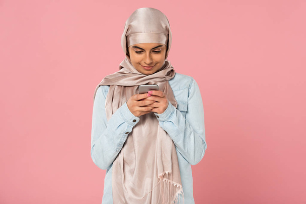 pembe izole akıllı telefon kullanarak gülümseyen müslüman kız - Fotoğraf, Görsel