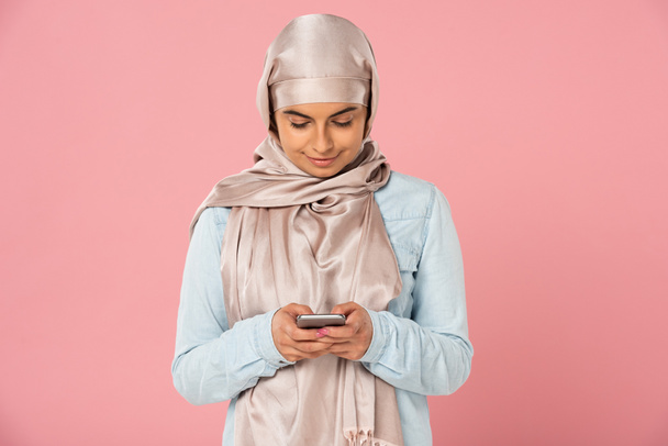 красива усміхнена мусульманська дівчина використовує смартфон ізольовано на рожевому
 - Фото, зображення