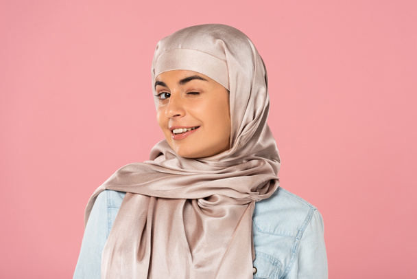 portrait of beautiful muslim girl in hijab winking isolated on pink - Zdjęcie, obraz