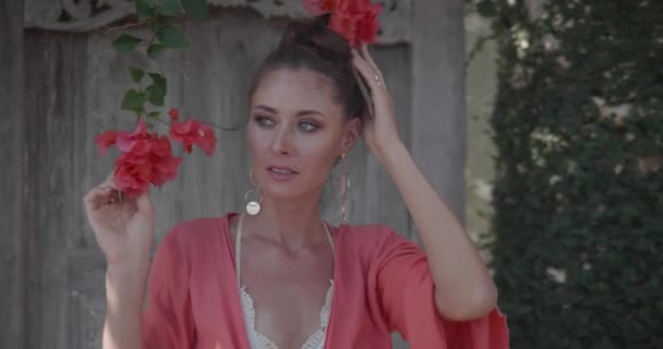 Porträt einer schönen Frau, die im Garten mit Blumen neben dem hölzernen Tor posiert - Video in Zeitlupe - Filmmaterial, Video