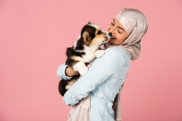 Arabisch meisje in hijab houden schattige Corgi puppy, geïsoleerd op roze - Foto, afbeelding
