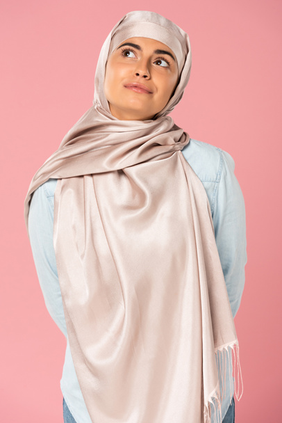 attractive dreamy muslim woman in hijab, isolated on pink  - Zdjęcie, obraz