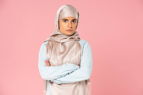 attractive skeptical arabic girl in hijab with crossed arms, isolated on pink  - Photo, Image