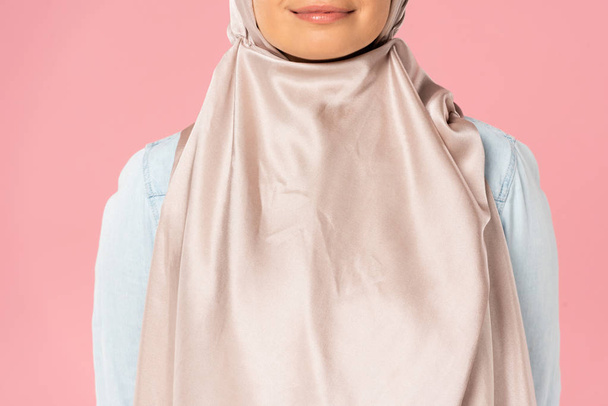 oříznutý pohled na krásnou usmívající se muslimskou dívku v hidžábu, izolovaný na růžovém - Fotografie, Obrázek