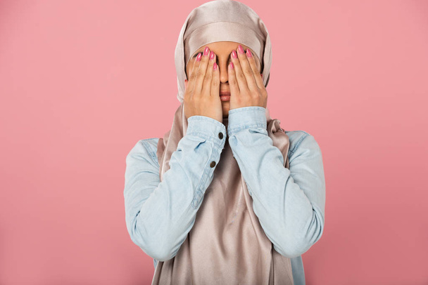 ヒジャーブの目を閉じて美しい怖いイスラム教徒の女の子, ピンクに隔離 - 写真・画像