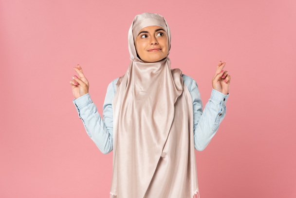 šťastná muslimka v hidžábu s prsty zkřížené, izolovaná na růžovém  - Fotografie, Obrázek