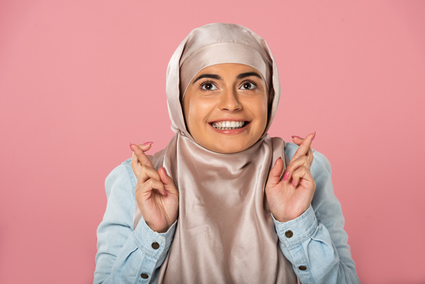 指を交差させたヒジャーブの陽気なイスラム教徒の女性は、ピンクで隔離  - 写真・画像