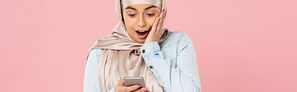 wstrząśnięty muzułmaninem dziewczyna w hidżab za pomocą smartfona na białym tle - Zdjęcie, obraz