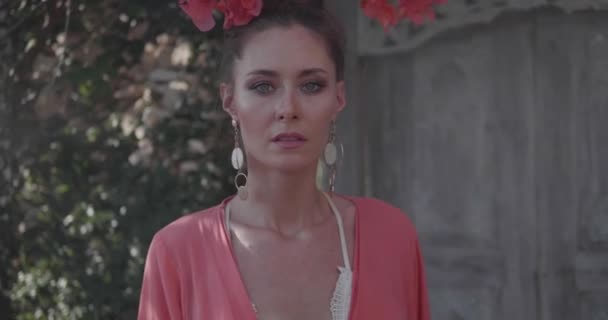 Portrait of beautiful woman posing in the garden with flowers near the wooden door gate - video in slow motion - Footage, Video