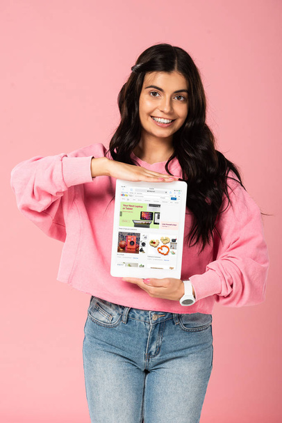 KYIV, UKRAINE HEINÄKUU 30, 2019: hymyilevä tyttö, jolla on digitaalinen tabletti, jossa on eBay-sovellus näytöllä, eristetty vaaleanpunaisella
 - Valokuva, kuva