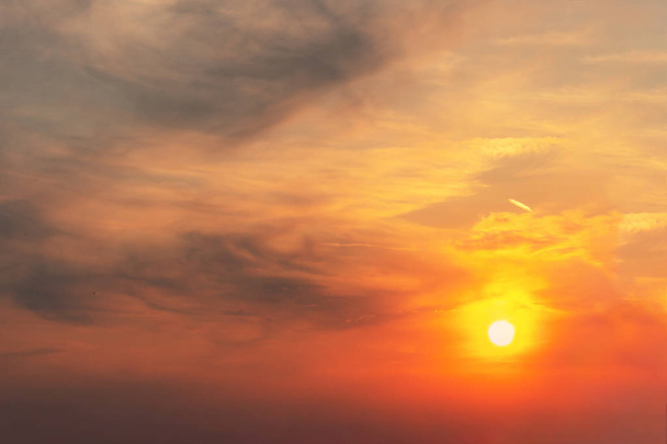 Il tramonto nel cielo è rosso-arancio con nuvole grigie sotto forma di macchie su cui splende il sole
. - Foto, immagini