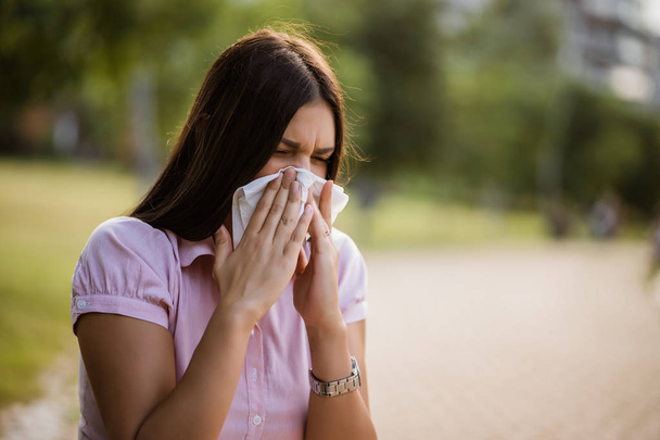 Woman with allergy symptom blowing nose in park. - Photo, Image