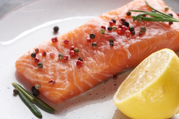 закрыть вид сырого свежего лосося с перцем, лимоном и розмарином на тарелке
 - Фото, изображение
