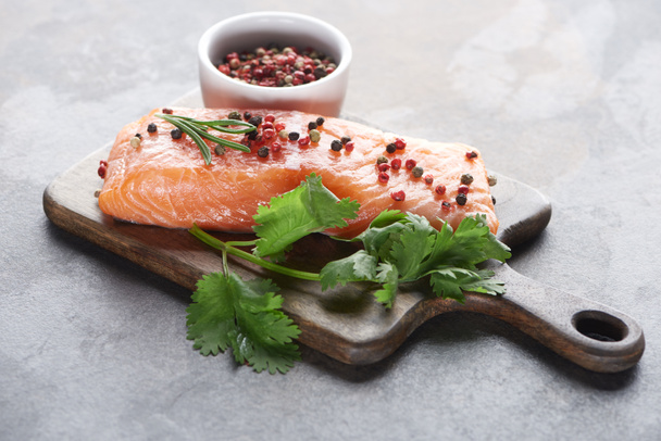 raw fresh salmon with peppercorns, parsley and rosemary on wooden cutting board - Photo, Image