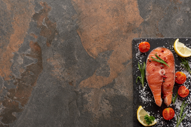 Ansicht von rohem Lachs mit Gewürzen und Tomaten auf Steinplatte - Foto, Bild