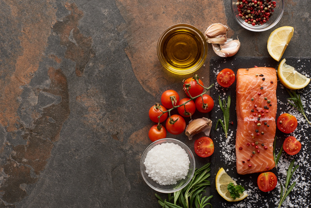 top view of raw salmon with seasoning, oil, garlic and tomatoes on stone surface - Fotoğraf, Görsel