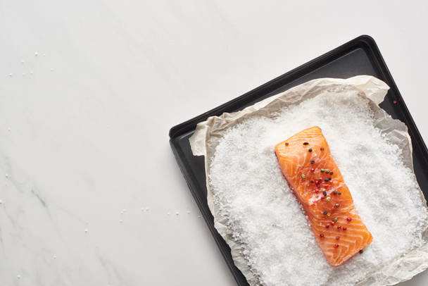 vista superior del filete de salmón crudo con pimienta en la bandeja del horno con sal en la superficie de mármol
 - Foto, imagen