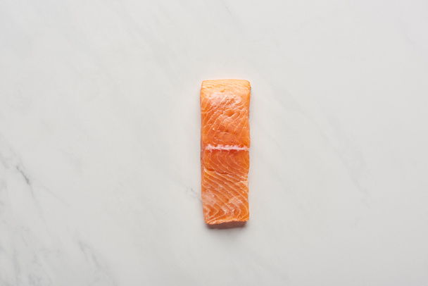 top view of uncooked fresh salmon steak on white marble surface - Fotó, kép