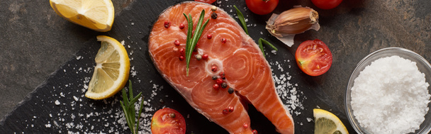 top view of raw salmon steak with salt, lemon and tomatoes on stone board, panoramic shot - Foto, Imagem