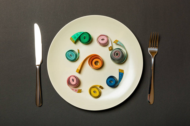 Maßband in einem Teller mit Gabel und Messer auf beiden Seiten auf schwarzem Hintergrund. Ansicht des Gewichtsverlust-Konzepts - Foto, Bild