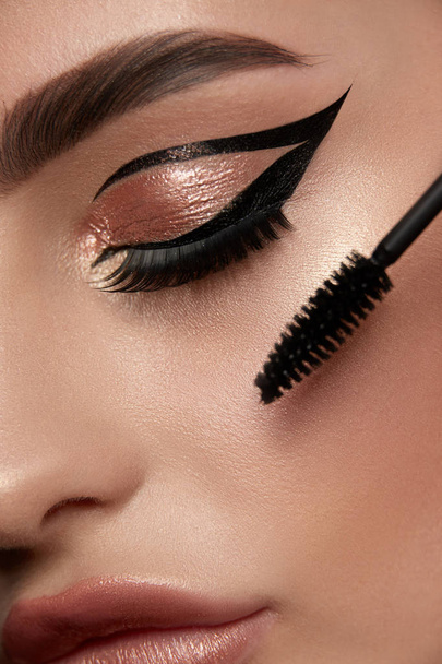 close-up de olho de mulher com delineador e sombra dourada e escova de rímel, conceito de maquiagem dourada de luxo
  - Foto, Imagem