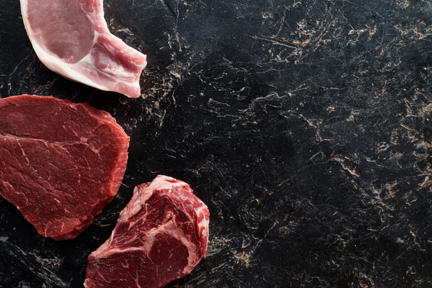 黒い大理石の表面に生の牛肉と豚肉の部分のトップビュー - 写真・画像