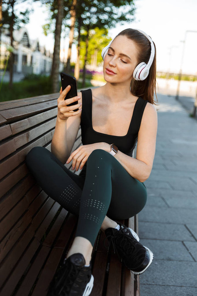 Image of athletic sportswoman holding smartphone and listening t - Φωτογραφία, εικόνα