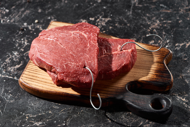 wooden cutting board with raw beef steaks on black marble surface - Photo, Image