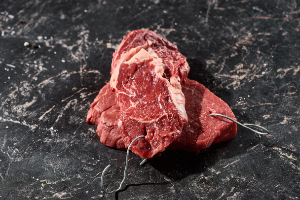 сирі частини яловичини з гачками на поверхні чорного мармуру
 - Фото, зображення
