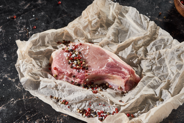 raw pork steak sprinkled with salt and pepper on parchment paper on black marble surface - Photo, Image