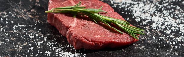 panoramic shot of unprocessed beef steak with rosemary on black marble surface with scattered salt - Φωτογραφία, εικόνα