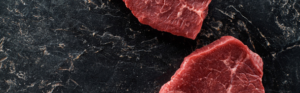 panoramic shot of unprocessed beef steaks on black marble surface - Фото, изображение