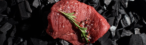 panoramic shot of raw beef sirloin with rosemary, salt and pepper on coal pieces - Photo, Image