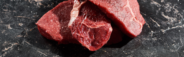 панорамний знімок сирих шматочків яловичини один на одному на поверхні чорного мармуру
 - Фото, зображення