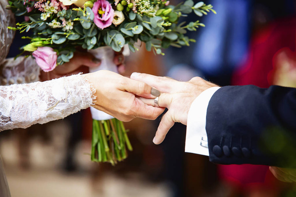 Рука невесты надевает обручальное кольцо на палец жениха
 - Фото, изображение