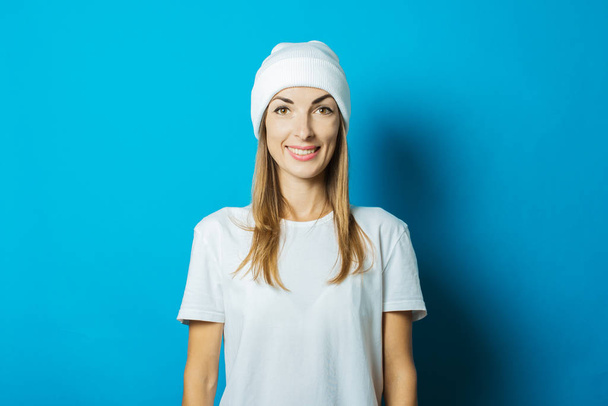 Fiatal nő, fehér kalap és póló mosolyogva a kék háttér - Fotó, kép