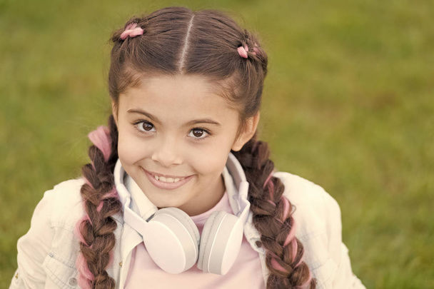 Healthy emotional happy kid relaxing outdoors. What makes child happy. Girl braids hairstyle and modern headphones enjoy relax. Secrets to raising happy child. Girl cute kid green grass background - Foto, Bild