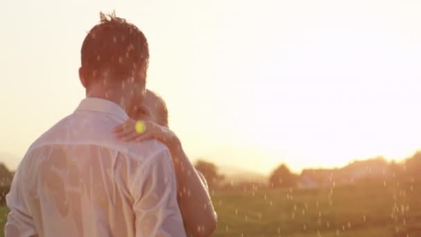 Pomalý pohyb uzavření rozptylového skla: krásný Kavkazský pár si nevšímá, když tančí ve sprše na malebném letním venkově. Veselá přítelkyně a přítel se točí v dešti. - Záběry, video