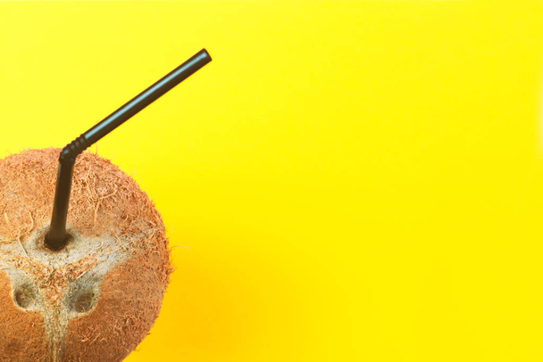 Coconut with black straw on neon bright yellow background in vaporwave webpunk style, top view with free copy space for text. Summer concept tropical flat lay. Fashion minimalism surrealism in fruits  - Photo, Image