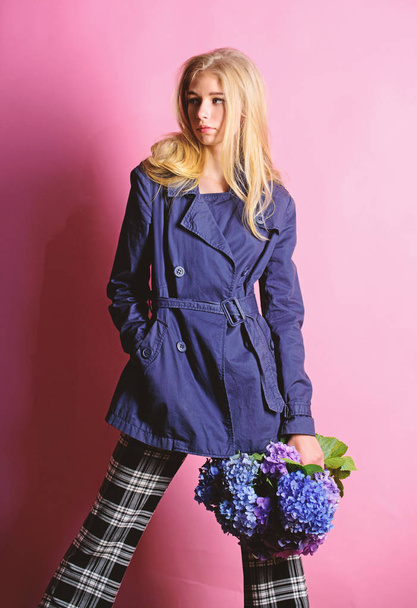 Must have concept. Fashionable coat. Woman blonde hair posing coat with flowers bouquet. Clothes and accessory. Girl fashion model wear coat for spring and autumn season. Trench coat fashion trend - Фото, изображение