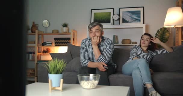 Girl and guy watching TV at night with sad faces, guy wiping eyes with tissue - Filmagem, Vídeo