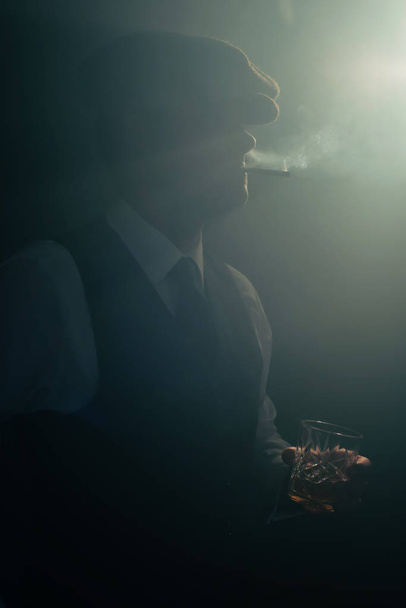 Retro zakenman met Cap rookt sigaret in rokerige kamer. - Foto, afbeelding