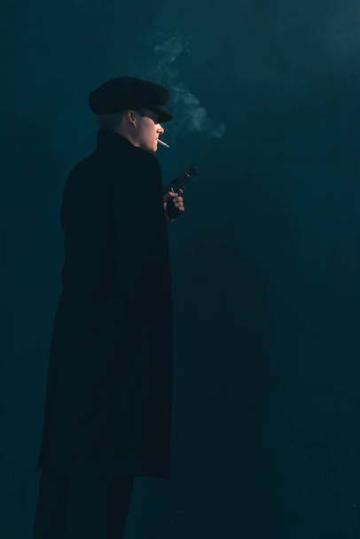 Um mafioso retrô com um cigarro segura uma arma. Vista lateral
. - Foto, Imagem