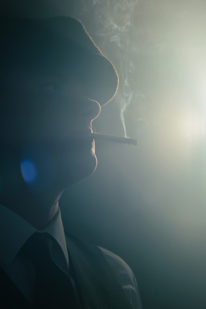 Retro-Mann mit Mütze raucht Zigarette im verrauchten Raum. Seitenansicht. - Foto, Bild