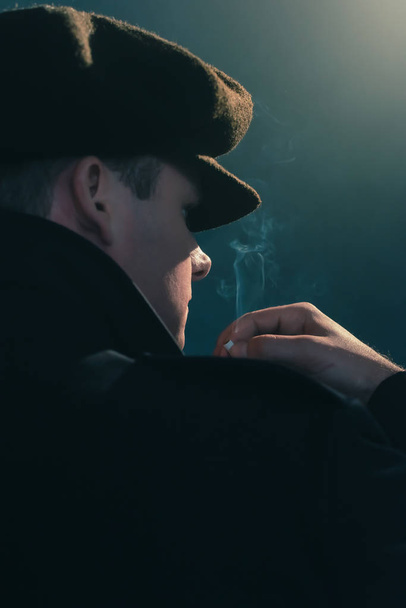 キャップを持つレトロな男は、煙の部屋でタバコを吸います。側面図. - 写真・画像