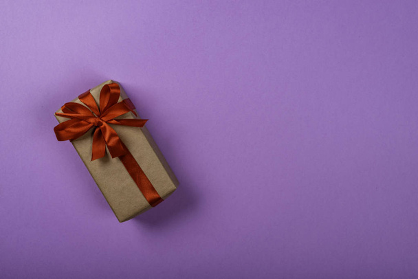Caja de regalo con lazo sobre fondo de neón púrpura. Espacio para texto en el lado derecho de la imagen
. - Foto, imagen