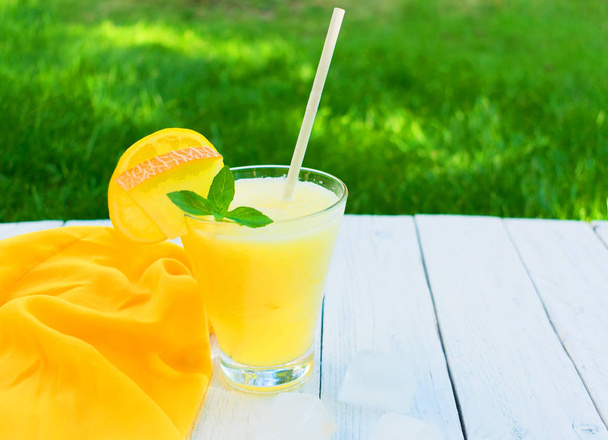 Bright melon smoothie with mint and lemon on a background of fresh green grass. Copy space. Concept of summer cooling drinks. - Photo, Image