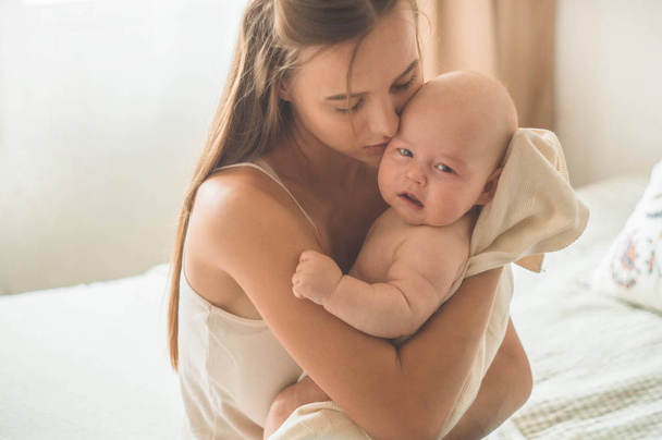 Porträt eines Neugeborenen mit Mutter auf dem Bett. Mutter hält und küsst ihr Kind. - Foto, Bild