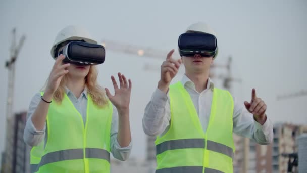 Два человека в очках виртуальной реальности на фоне строящихся зданий с кранами имитируют работу интерфейса для контроля и управления строительством
 - Кадры, видео