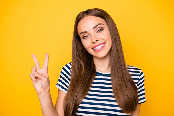 Close up photo of sweet lady making v-signs looking at camera smiling wearing striped t-shirt isolated over yellow background - Foto, Bild